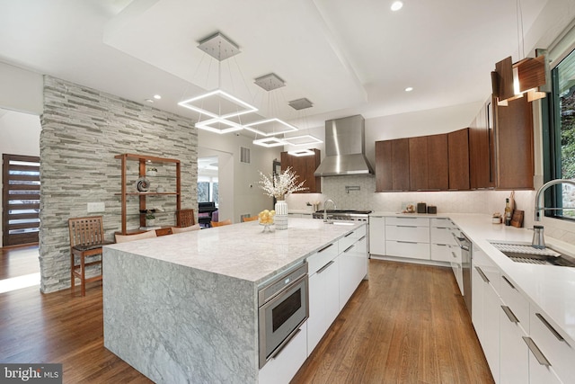 kitchen featuring dark wood-style flooring, a sink, stainless steel appliances, wall chimney exhaust hood, and modern cabinets