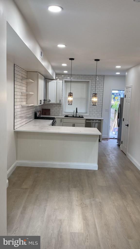 kitchen featuring appliances with stainless steel finishes, tasteful backsplash, hanging light fixtures, kitchen peninsula, and white cabinets