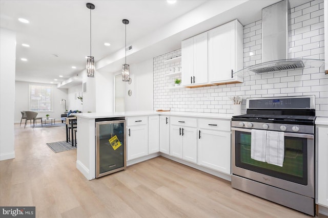 kitchen with wall chimney exhaust hood, stainless steel gas range oven, light hardwood / wood-style flooring, beverage cooler, and white cabinets