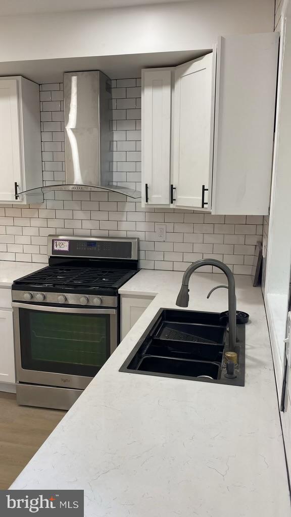 kitchen featuring light wood-type flooring, stainless steel range with gas cooktop, white cabinetry, sink, and wall chimney exhaust hood