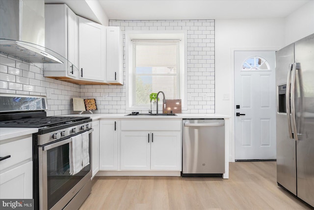 kitchen with white cabinets, light hardwood / wood-style flooring, appliances with stainless steel finishes, sink, and wall chimney exhaust hood