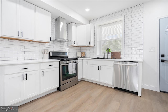 kitchen featuring stainless steel appliances, sink, light wood-type flooring, white cabinetry, and wall chimney range hood