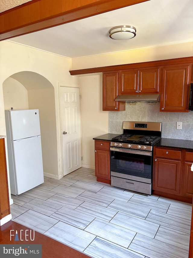 kitchen with dark stone countertops, white fridge, stainless steel gas range, and tasteful backsplash