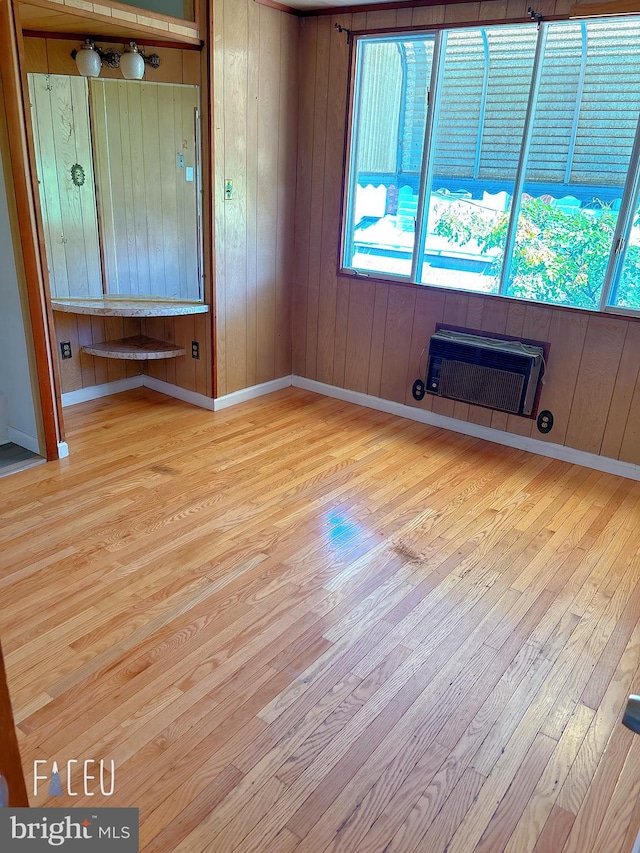 unfurnished bedroom with light hardwood / wood-style flooring, wooden walls, and heating unit