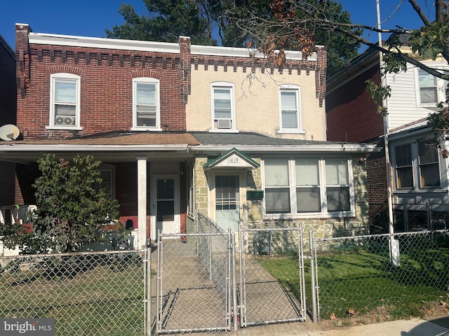 townhome / multi-family property with a porch, a gate, stone siding, and a fenced front yard