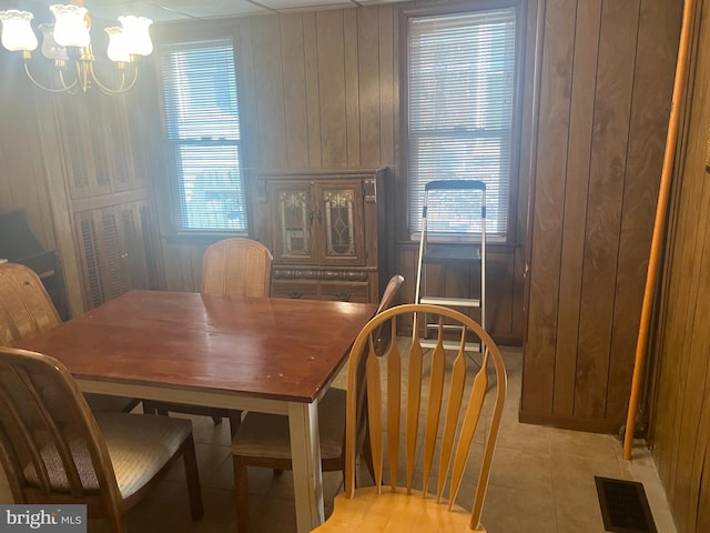 dining area featuring plenty of natural light, wood walls, an inviting chandelier, and light tile patterned flooring