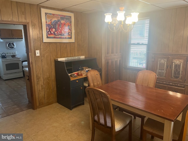 dining room with wood walls, a paneled ceiling, and an inviting chandelier