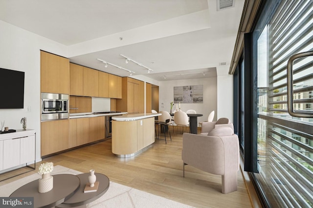 kitchen featuring stainless steel microwave, light brown cabinetry, a center island, and light hardwood / wood-style floors