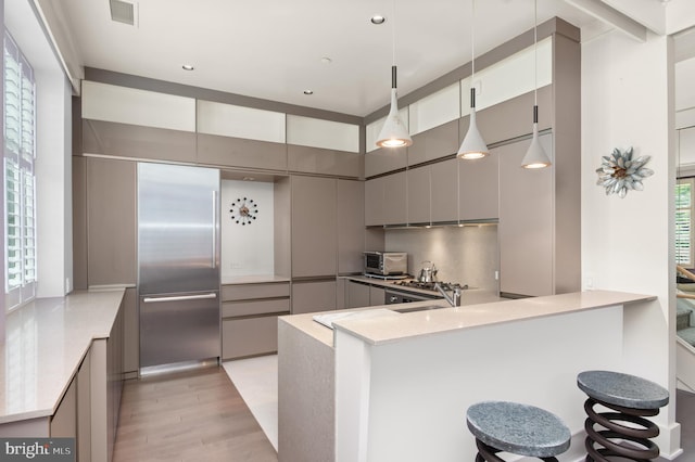 kitchen featuring hanging light fixtures, light wood-type flooring, built in fridge, kitchen peninsula, and a kitchen bar