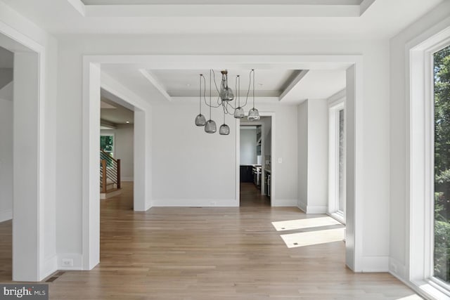 unfurnished dining area featuring a raised ceiling, an inviting chandelier, and light wood-type flooring