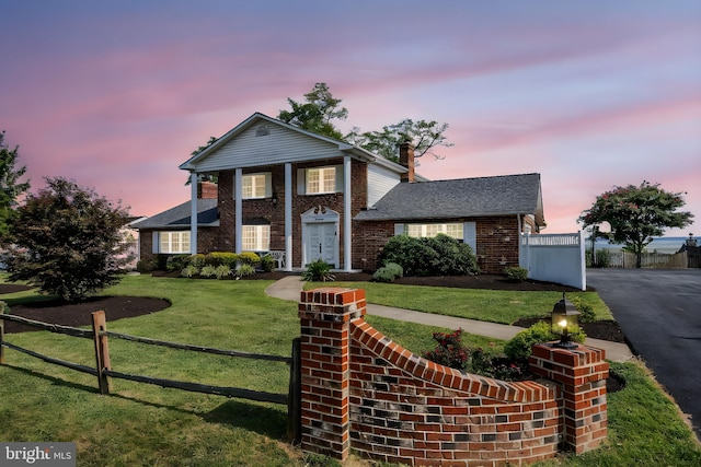 view of front facade with brick siding, aphalt driveway, a yard, and fence