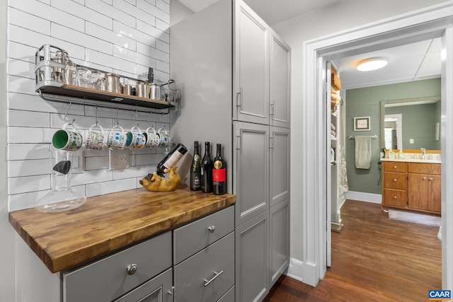 bar with gray cabinets, wooden counters, sink, decorative backsplash, and dark wood-type flooring