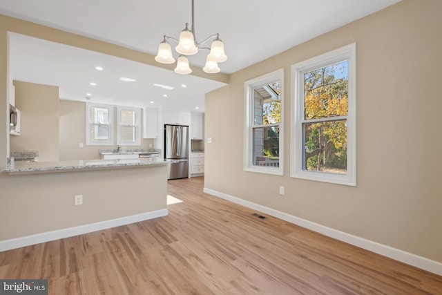 kitchen featuring stainless steel appliances, kitchen peninsula, decorative light fixtures, white cabinets, and light wood-type flooring