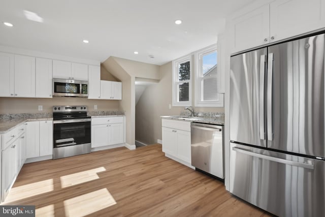 kitchen featuring light wood-type flooring, appliances with stainless steel finishes, light stone counters, and white cabinets