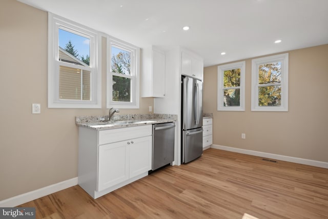 kitchen featuring white cabinetry, light wood-type flooring, appliances with stainless steel finishes, and light stone counters