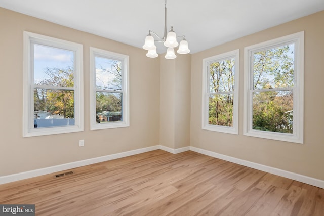 empty room with a healthy amount of sunlight, light hardwood / wood-style flooring, and a notable chandelier