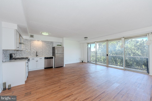 kitchen featuring light wood finished floors, a sink, backsplash, stainless steel appliances, and light countertops