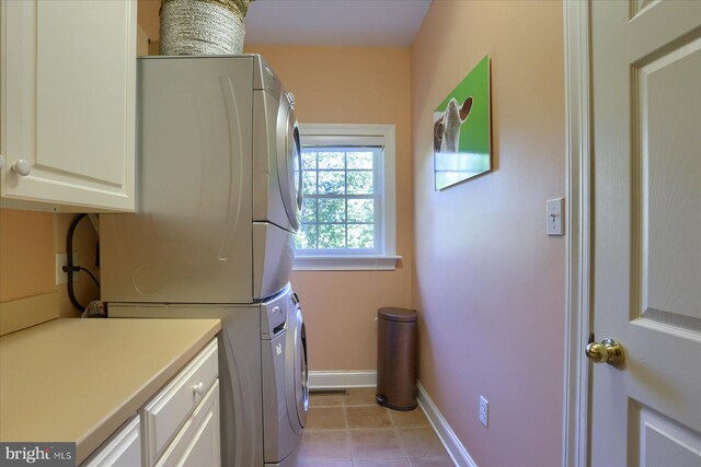 clothes washing area with cabinets, light tile patterned floors, and stacked washing maching and dryer