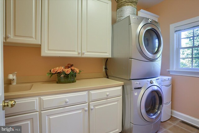 washroom with light tile patterned floors, cabinets, sink, and stacked washer and dryer