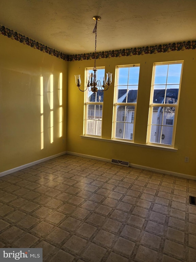 unfurnished dining area featuring visible vents, baseboards, a textured ceiling, and an inviting chandelier