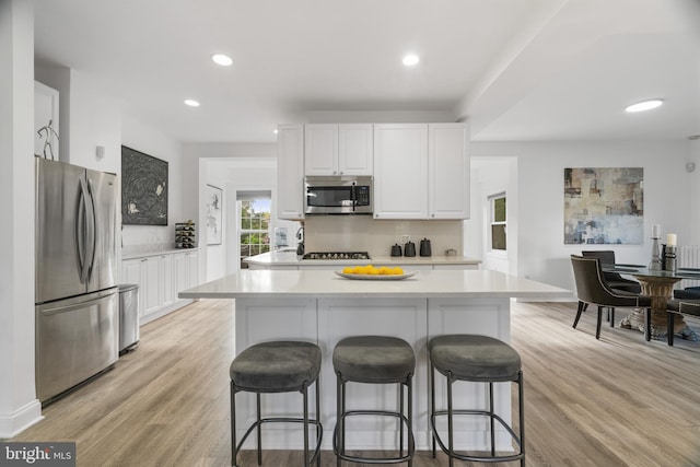 kitchen featuring white cabinets, stainless steel appliances, a breakfast bar, light wood-type flooring, and decorative backsplash