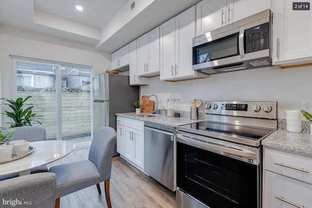 kitchen featuring light stone countertops, light wood-type flooring, appliances with stainless steel finishes, white cabinetry, and a sink