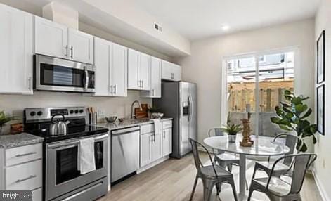 kitchen with light wood-type flooring, white cabinetry, stainless steel appliances, and light stone countertops