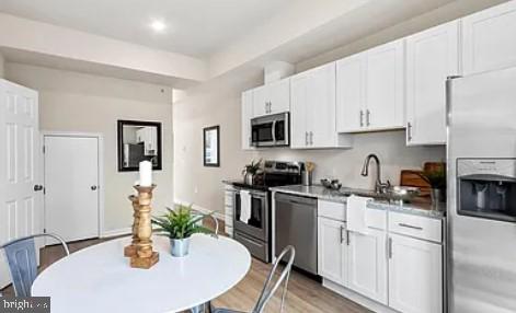 kitchen with sink, stainless steel appliances, white cabinets, and light hardwood / wood-style floors