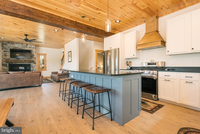 kitchen with a stone fireplace, appliances with stainless steel finishes, custom range hood, and white cabinets