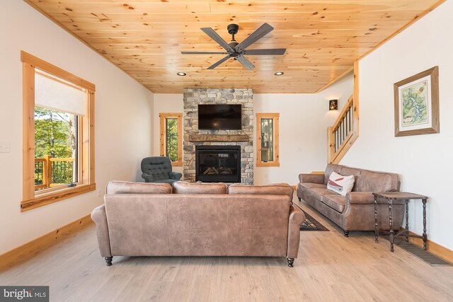 living room with light hardwood / wood-style flooring, wood ceiling, ceiling fan, and a stone fireplace