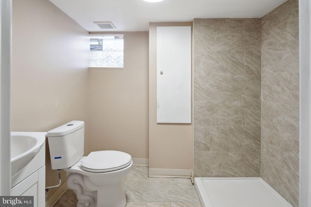 bathroom featuring toilet, a tile shower, and vanity