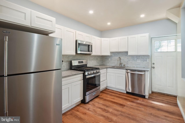 kitchen with white cabinetry, tasteful backsplash, sink, appliances with stainless steel finishes, and hardwood / wood-style flooring