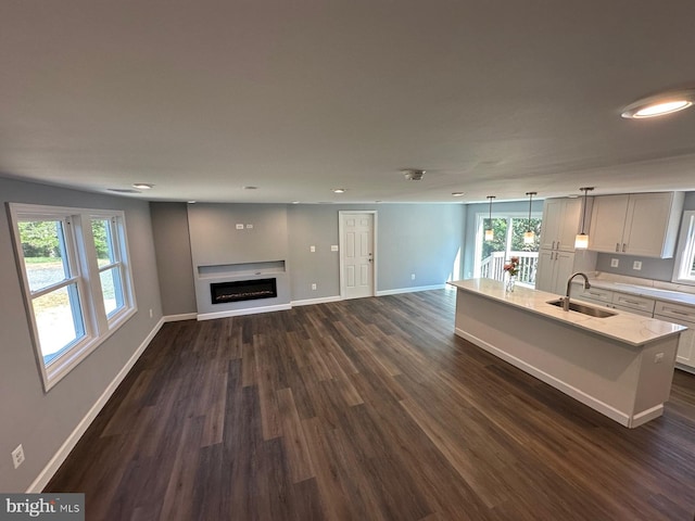 kitchen with dark wood-type flooring, a center island with sink, decorative light fixtures, and a healthy amount of sunlight