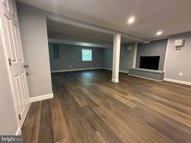 basement featuring a brick fireplace, electric panel, and dark hardwood / wood-style flooring