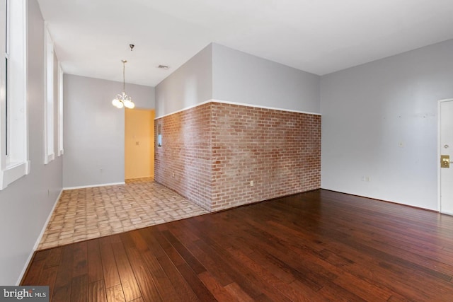 spare room with wood-type flooring, brick wall, and a notable chandelier