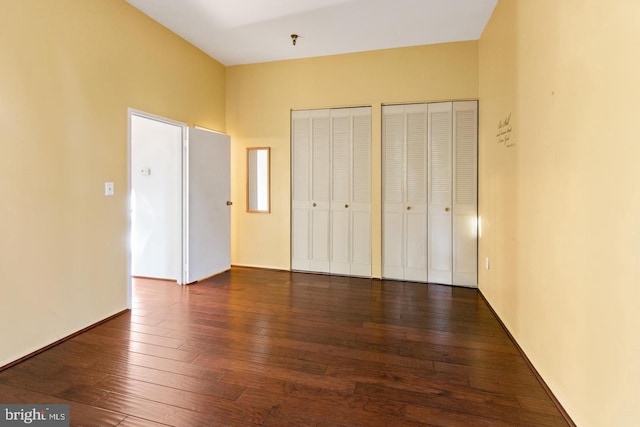 unfurnished bedroom featuring dark wood-type flooring and two closets