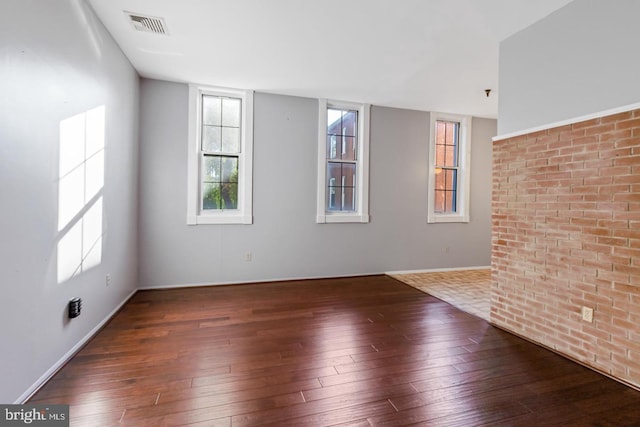 spare room featuring dark hardwood / wood-style flooring and brick wall