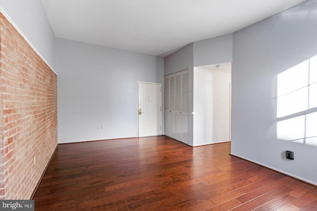 unfurnished room featuring dark wood-type flooring and brick wall