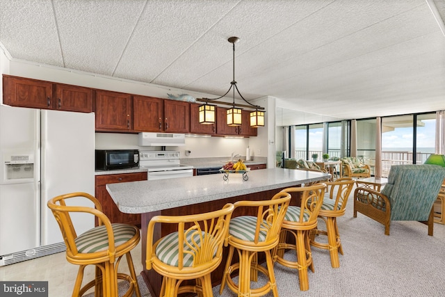 kitchen featuring decorative light fixtures, a wall of windows, white appliances, a breakfast bar area, and a kitchen island