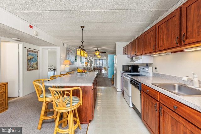 kitchen featuring a sink, under cabinet range hood, open floor plan, white appliances, and a breakfast bar area