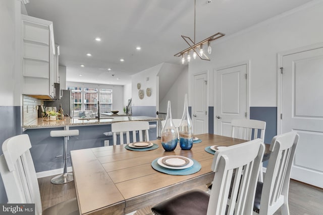 dining area with light wood-type flooring, ornamental molding, sink, and a notable chandelier