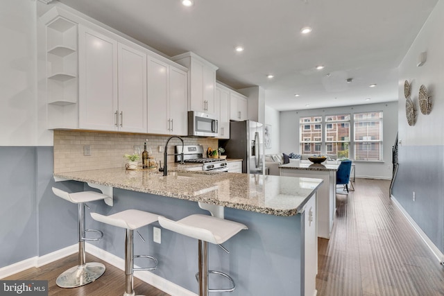 kitchen featuring white cabinets, kitchen peninsula, stainless steel appliances, dark hardwood / wood-style floors, and a kitchen bar