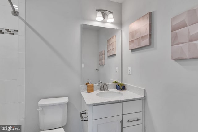 bathroom with a tile shower, vanity, and toilet