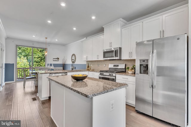 kitchen featuring white cabinets, kitchen peninsula, a kitchen island, appliances with stainless steel finishes, and decorative light fixtures