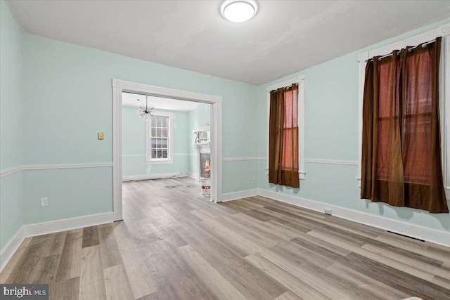 unfurnished room with a notable chandelier and light wood-type flooring