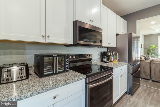 kitchen featuring light wood-type flooring, stainless steel appliances, white cabinetry, and light stone countertops