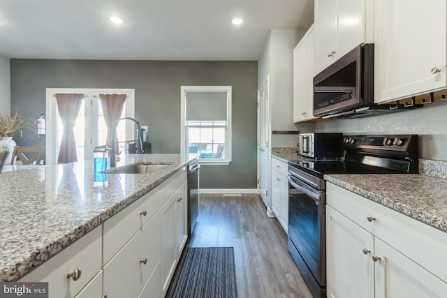 kitchen with light stone countertops, white cabinets, appliances with stainless steel finishes, dark hardwood / wood-style flooring, and sink