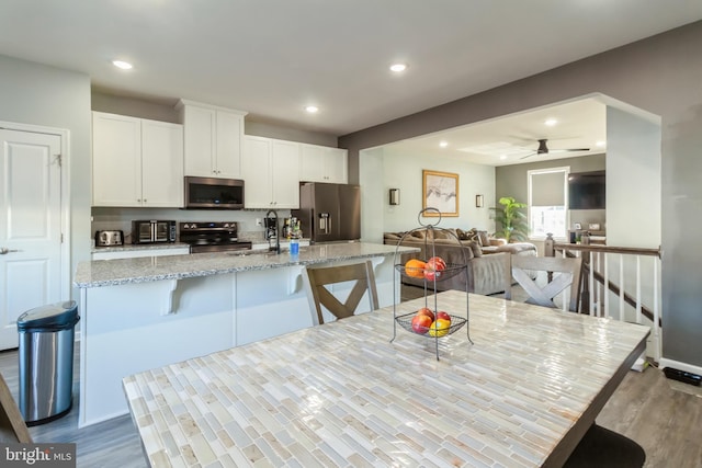 kitchen with ceiling fan, appliances with stainless steel finishes, a kitchen breakfast bar, light stone countertops, and white cabinets