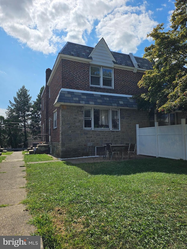 back of house with fence, a high end roof, a lawn, a chimney, and stone siding