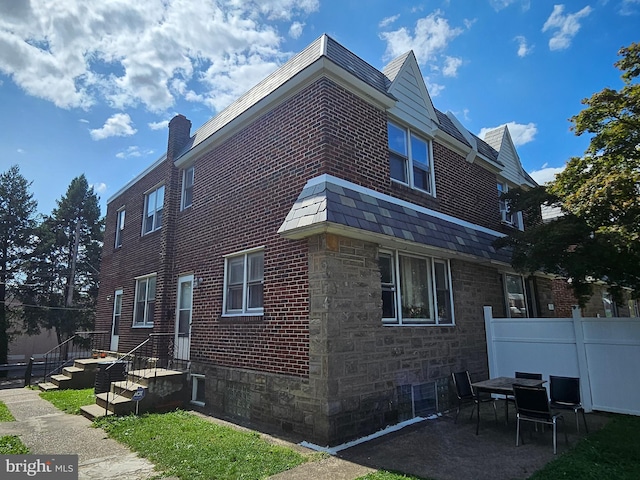 view of side of home featuring stone siding, brick siding, a chimney, and fence